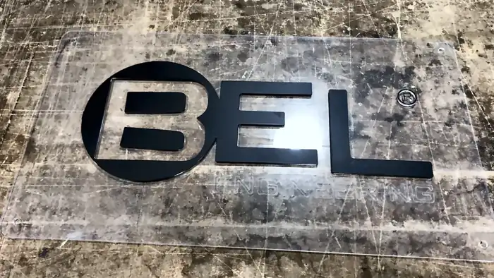 Logo BEL cortado en acrílico negro sobre placa transparente